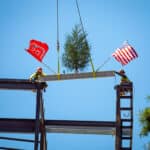 Two workers place a steel beam completing the bones of NC State’s Integrative Sciences Building.