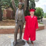 Poole graduate Bob Schwartz in his red robes posing with the statue of Jim Valvano.