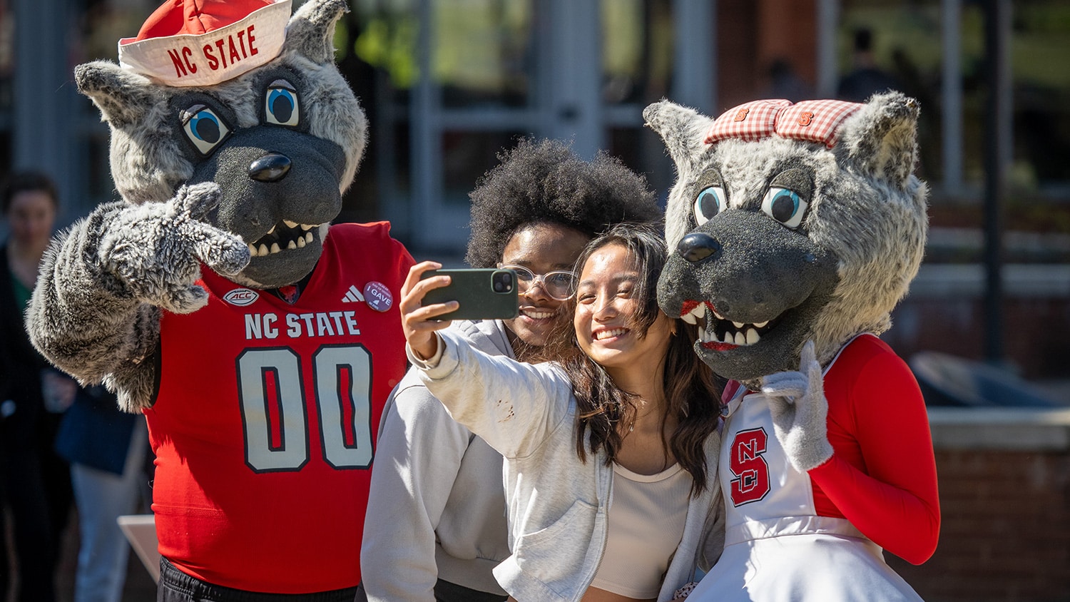 Two students take a selfie with Mr. and Ms. Wuf on Day of Giving.