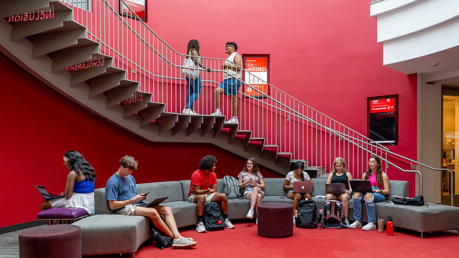 Students gather on a long couch positioned below a curving set of stairs in Talley Student Union.