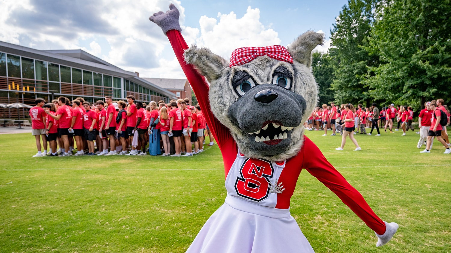 Ms. Wuf poses for a photo with a crowd of students in red T-shirts behind her.