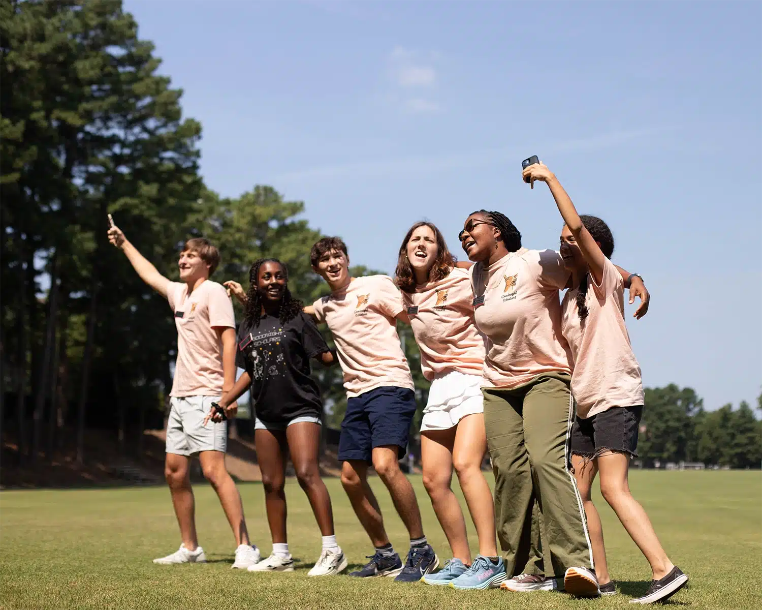 Six students chant together outside, arms around each other, on a sunny day. 